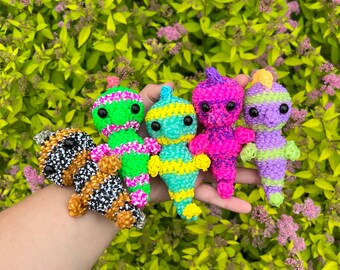 May include: Five colorful rubber band bracelets in the shape of cartoon characters. The bracelets are green, yellow, pink, purple, and black and white.