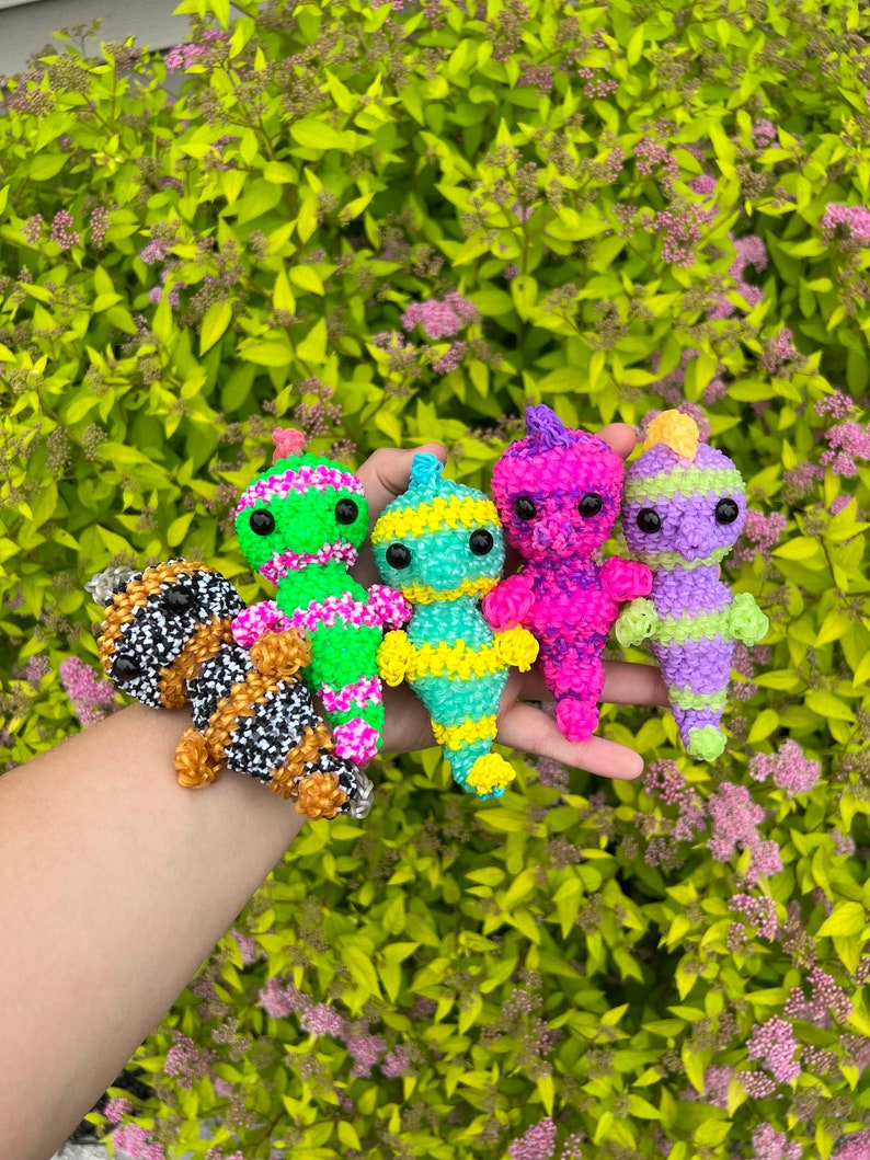 Puede incluir: Cinco pulseras de gomas el&aacute;sticas de colores con forma de personajes de dibujos animados. Las pulseras son verdes, amarillas, rosas, moradas y blancas y negras.