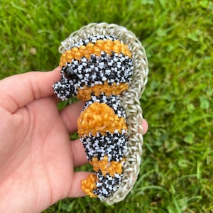 Puede incluir: Una peque&ntilde;a figura de caballito de mar hecha a mano con gomas el&aacute;sticas de colores. El caballito de mar es negro, blanco y naranja con una cola de goma el&aacute;stica blanca y transparente.