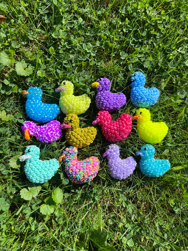 May include: A collection of 12 colorful rubber band duck toys. The ducks are made of rainbow loom rubber bands and are in various colors, including blue, green, purple, yellow, and red.