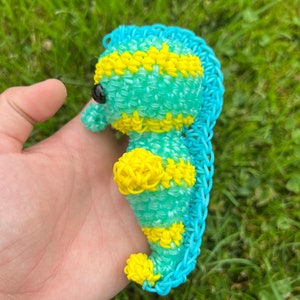 Puede incluir: Un caballito de mar de gomas el&aacute;sticas azul y amarillo. El caballito de mar est&aacute; hecho de peque&ntilde;as gomas el&aacute;sticas entrelazadas. El caballito de mar tiene una cola amarilla y un cuerpo azul con rayas amarillas.