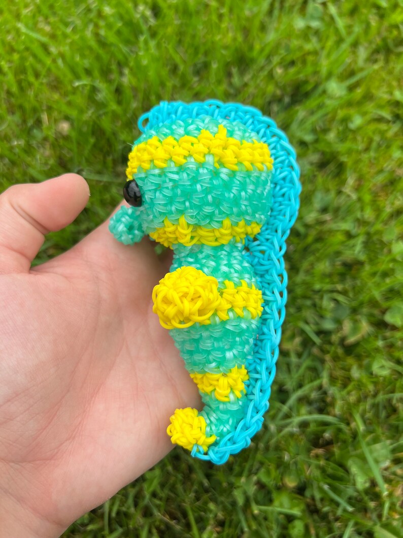 Puede incluir: Un caballito de mar de gomas el&aacute;sticas azul y amarillo. El caballito de mar est&aacute; hecho de peque&ntilde;as gomas el&aacute;sticas entrelazadas. El caballito de mar tiene una cola amarilla y un cuerpo azul con rayas amarillas.