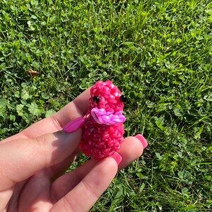May include: A pink rubber band animal with black eyes and a pink mouth. The animal is made of rubber bands and is about the size of a small apple.