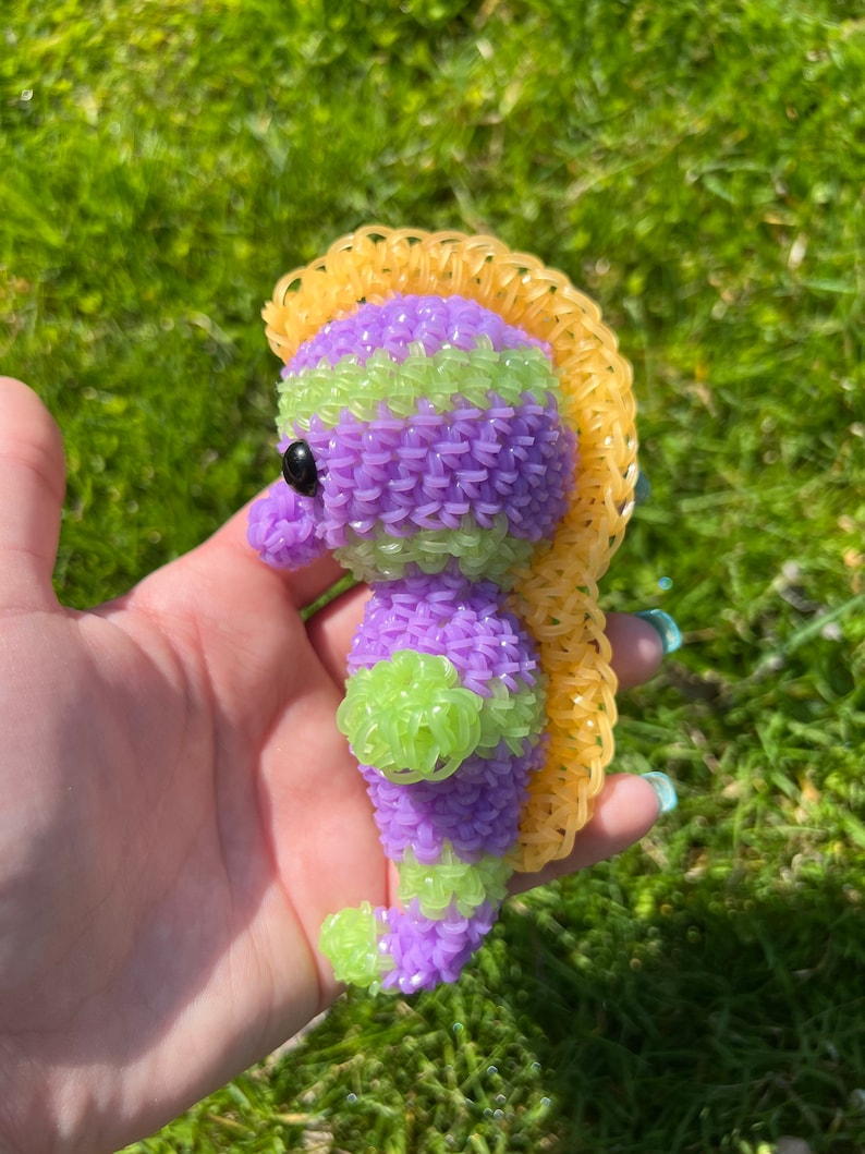 Puede incluir: Un caballito de mar de gomas el&aacute;sticas moradas y verdes con una crin de gomas el&aacute;sticas amarillas.