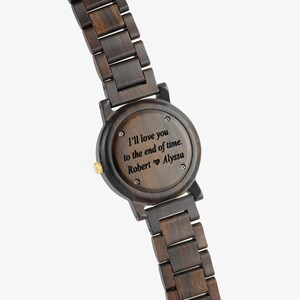 Puede incluir: Un reloj de pulsera de madera marr&oacute;n oscuro con un mensaje grabado en negro en la parte posterior: "I'll love you to the end of time. Robert &hearts; Alyssa"