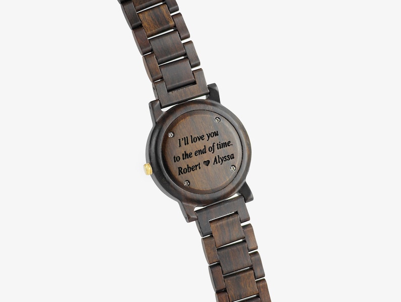 Puede incluir: Un reloj de pulsera de madera marr&oacute;n oscuro con un mensaje grabado en negro en la parte posterior: "I'll love you to the end of time. Robert &hearts; Alyssa"