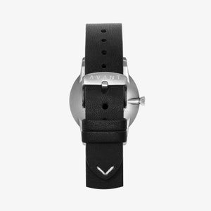 May include: A silver watch with a black leather band. The watch face is plain and the band has a white stitching detail. The watch has the word "AVANT" printed on the back.