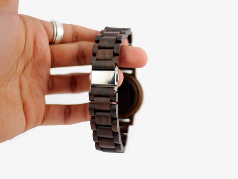 Puede incluir: Un reloj de pulsera de madera marr&oacute;n oscuro con un cierre plateado. La correa del reloj est&aacute; hecha de eslabones de madera individuales.