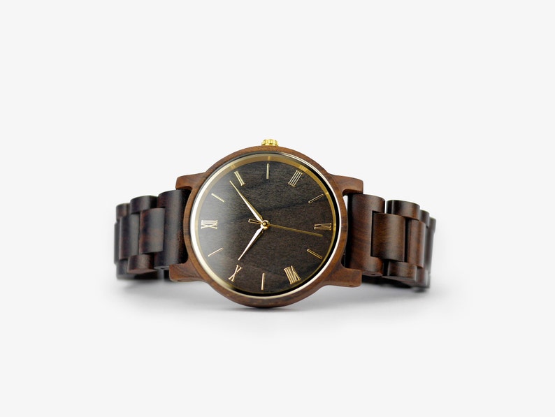 Puede incluir: Un reloj de pulsera de madera marr&oacute;n con una esfera negra y marcadores de hora en n&uacute;meros romanos dorados.