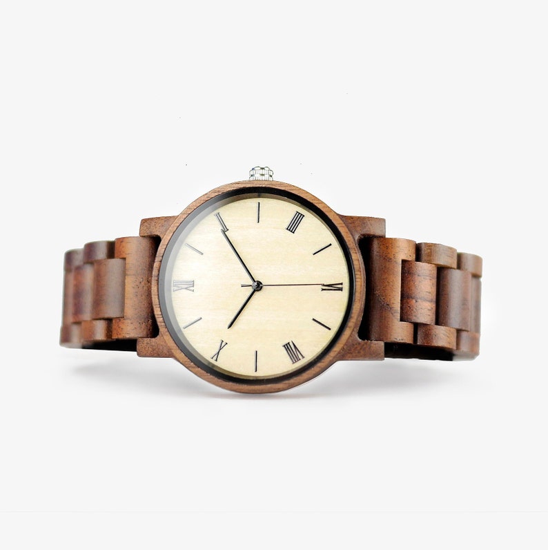 Puede incluir: Un reloj de pulsera de madera marr&oacute;n con una esfera de madera clara y marcadores de hora con n&uacute;meros romanos negros. El reloj tiene una correa de madera marr&oacute;n.