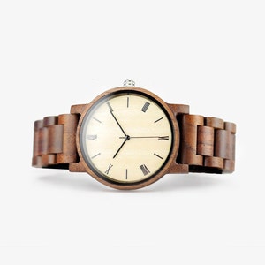 Puede incluir: Un reloj de pulsera de madera marr&oacute;n con una esfera marr&oacute;n claro y marcadores de hora en n&uacute;meros romanos negros. El reloj tiene una correa de madera marr&oacute;n.