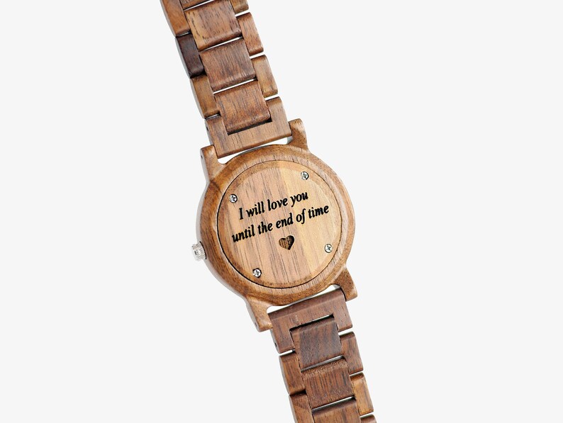 Puede incluir: Un reloj de pulsera de madera con una correa de madera marr&oacute;n y una esfera redonda. La parte posterior del reloj tiene un mensaje grabado que dice "Te amar&eacute; hasta el fin del tiempo" con un peque&ntilde;o s&iacute;mbolo de coraz&oacute;n.