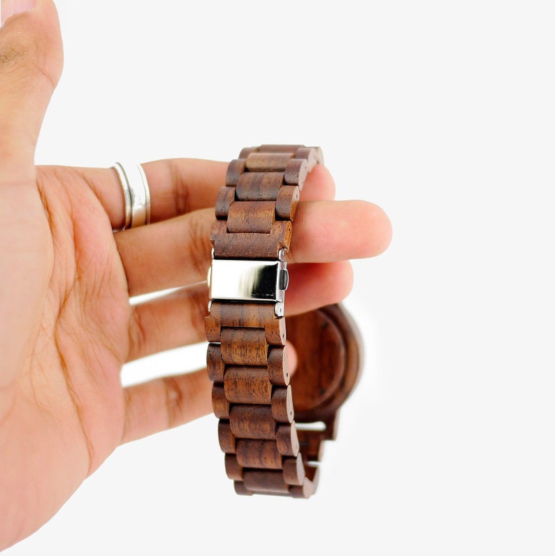 Puede incluir: Un reloj de madera marr&oacute;n con una hebilla plateada. La correa del reloj est&aacute; hecha de piezas de madera individuales.