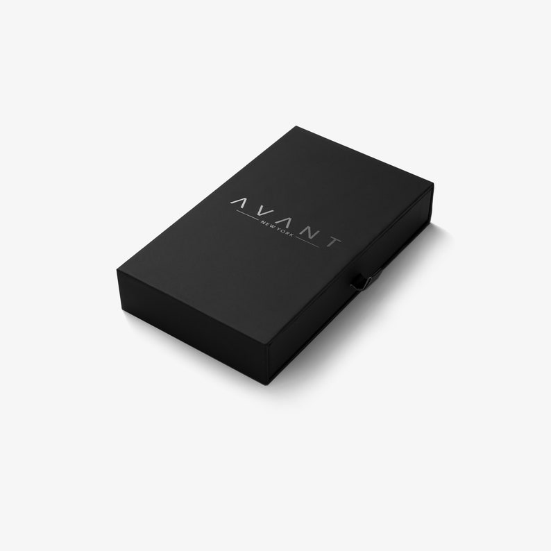 May include: A black rectangular box with the word "AVANT - NEW YORK" printed in silver. The box has a clasp on the right side and is set against a white background.