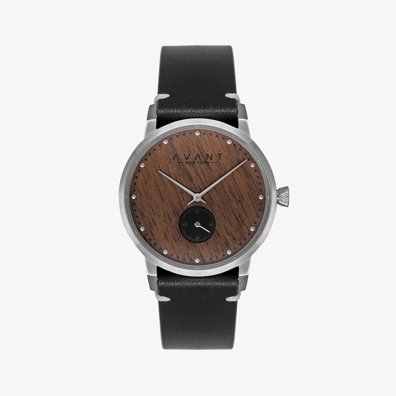 May include: A silver watch with a black leather band and a wooden face. The face has a wood grain pattern and the brand name "AVANT NEW YORK" is printed on it.