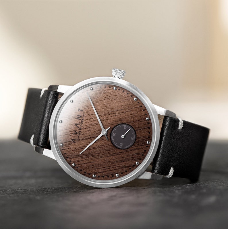 May include: A silver wristwatch with a black leather band. The watch face is made of wood with a small black dial for the seconds. The watch face has the text "ALTAN" written on it.