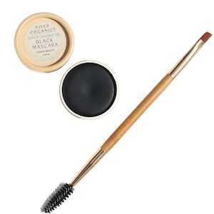 Puede incluir: Un peque&ntilde;o recipiente redondo de m&aacute;scara de pesta&ntilde;as negra con un cepillo aplicador de madera. El recipiente est&aacute; etiquetado como "River Organics Clay & Coconut Oil Black Mascara Vegan Beauty".