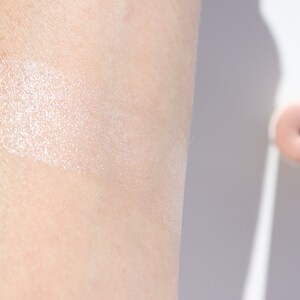 Natural cream highlighter swatch showing dewy ethereal glow on fair skin, organic illuminating makeup with rose quartz shimmer.