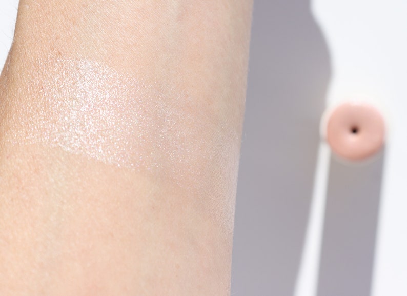 Natural cream highlighter swatch showing dewy ethereal glow on fair skin, organic illuminating makeup with rose quartz shimmer.