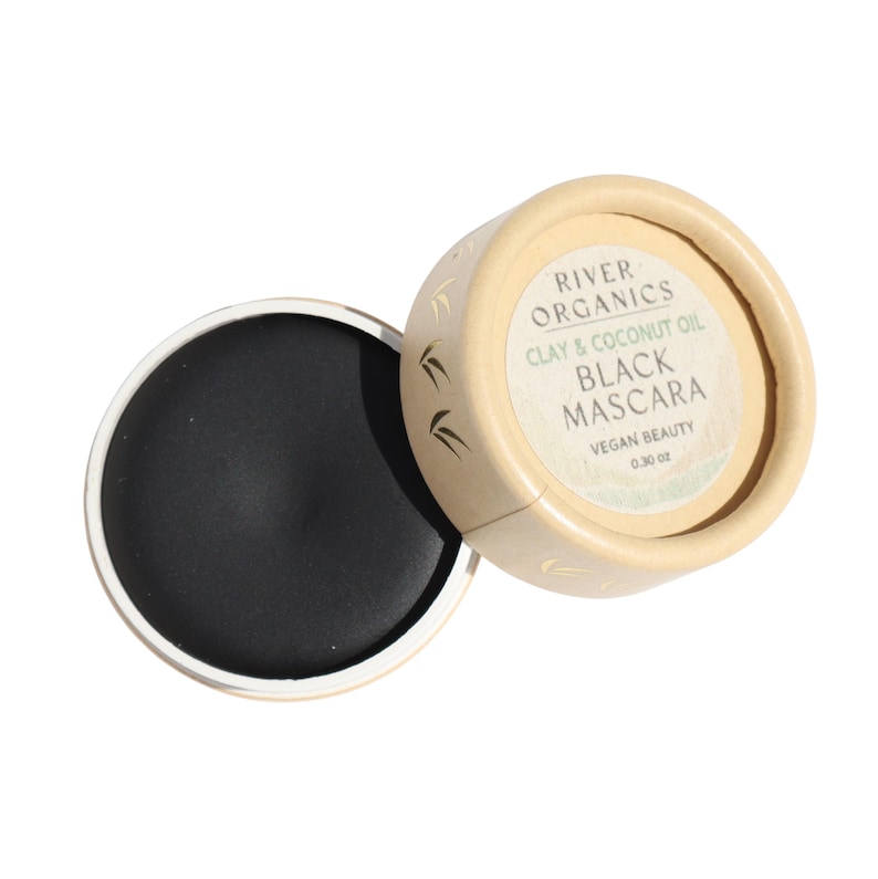 Puede incluir: Un peque&ntilde;o recipiente redondo beige con una tapa negra. El recipiente est&aacute; etiquetado como "River Organics Clay & Coconut Oil Black Mascara Vegan Beauty 0.30 oz".