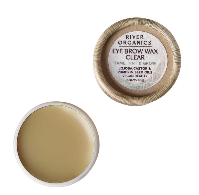 May include: Clear eye brow wax in a round container. The container has a cardboard exterior and a white interior. The text on the container reads "RIVER ORGANICS EYE BROW WAX CLEAR TAME, TINT & GROW" and lists ingredients and weight.