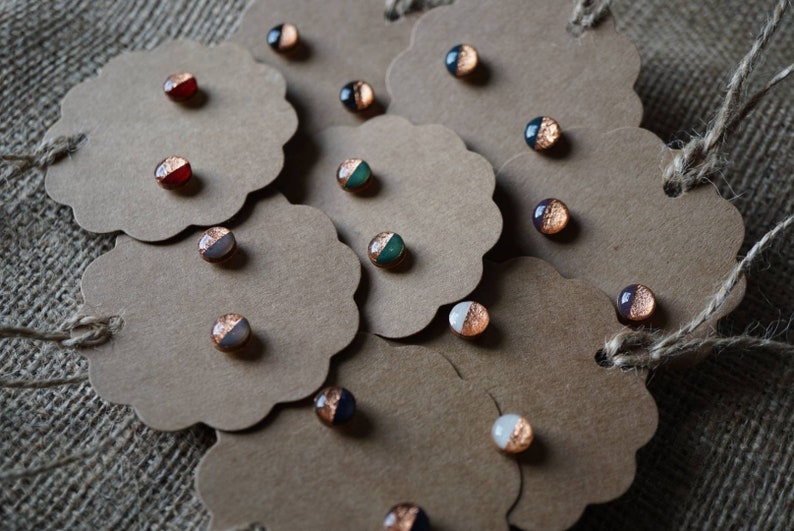 May include: Assortment of small, round, copper and glitter earrings displayed on brown paper cards. The earrings are in various colors, including red, green, white, and black.
