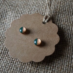 May include: A pair of small, round earrings with a green and gold design. The earrings are on a brown card with a scalloped edge.