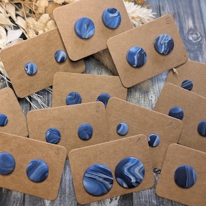 Könnte beinhalten: Eine Sammlung von Ohrsteckern aus blau-weißem Marmor, präsentiert auf braunen Ohrringkarten. Die Ohrringe haben ein Wirbelmuster und sind in verschiedenen Größen erhältlich. Sie sind auf einer Holzoberfläche angeordnet.