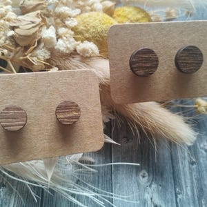 Op de afbeelding: Twee paar houten oorbellen op een bruine kaart. De oorbellen zijn rond en hebben een houtnerf.