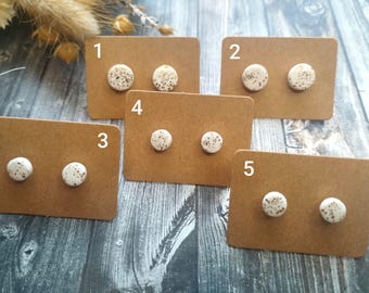 Puede incluir: Cinco tarjetas con los números del 1 al 5, cada una con dos pequeños pendientes redondos blancos con un patrón moteado. Los pendientes se muestran sobre una superficie marrón.