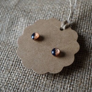 May include: A pair of small, round earrings with a black and copper design. The earrings are on a brown tag with a scalloped edge.