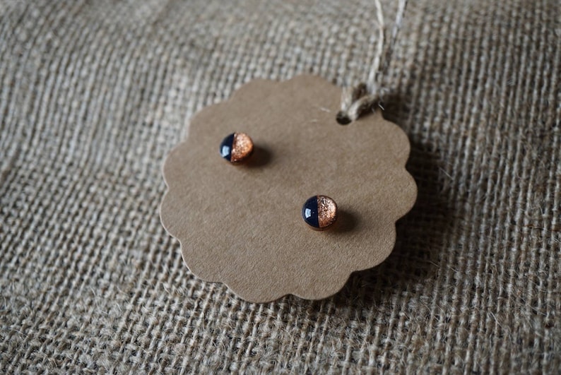 May include: A pair of small, round earrings with a black and copper design. The earrings are on a brown tag with a scalloped edge.