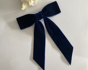 May include: A navy blue velvet bow with long tails. The bow is tied in a simple knot and the tails are long and flowing.