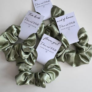 May include: Sage green satin scrunchies with white tags. Each tag has a different title: "bridesmaid", "maid of honour", "team bride", and "flower girl". The tags read "To have and to hold YOUR HAIR BACK" with a heart symbol.