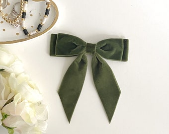 May include: A large, dark green velvet bow with a center knot. The bow is tied in a classic shape with two long tails.