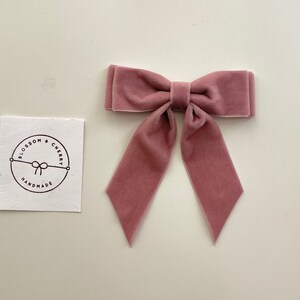 May include: A dusty rose velvet bow with long tails. The bow is handmade and has a simple, elegant design.