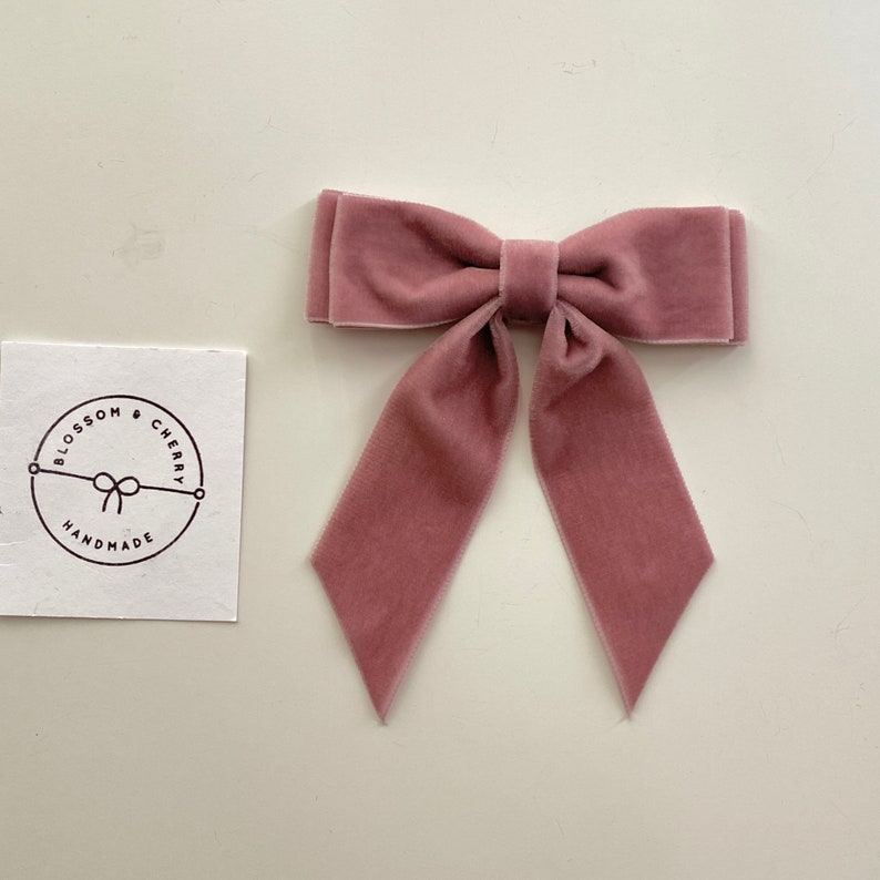 May include: A dusty rose velvet bow with long tails. The bow is handmade and has a simple, elegant design.
