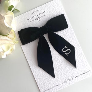 May include: Black velvet hair bow with a white embroidered letter "S" on one of the tails. The bow is handmade and is on a white card with the text "Handmade Blossom & Cherry" and the website address.