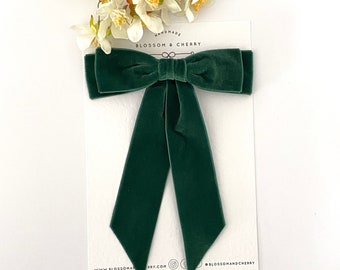 May include: A dark green velvet bow with long tails. The bow is handmade and is tied with a simple knot. The bow is on a white card with the text "Handmade Blossom & Cherry" printed on it.