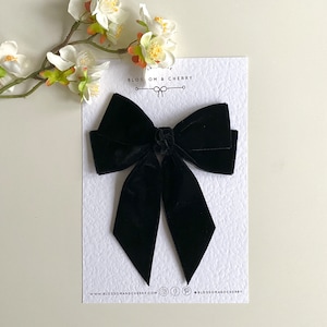 May include: A large black velvet bow with two long tails. The bow is on a white card with the text "BLOSSOM & CHERRY" and the website address "www.blossomandcherry.com".