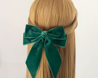 May include: A large green velvet bow hair clip. The bow is tied in a classic shape with two long tails.