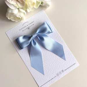 Op de afbeelding: Een lichtblauwe satijnen strik met een handgemaakt label met de tekst "Handmade Blossom & Cherry".