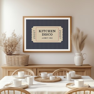 Puede incluir: Un cuadro enmarcado con un marco de madera marr&oacute;n que presenta un dise&ntilde;o de boleto que dice "KITCHEN DISCO ADMIT ONE" sobre un fondo a rayas azul marino. El cuadro se exhibe sobre un mueble de madera, con una mesa de comedor.
