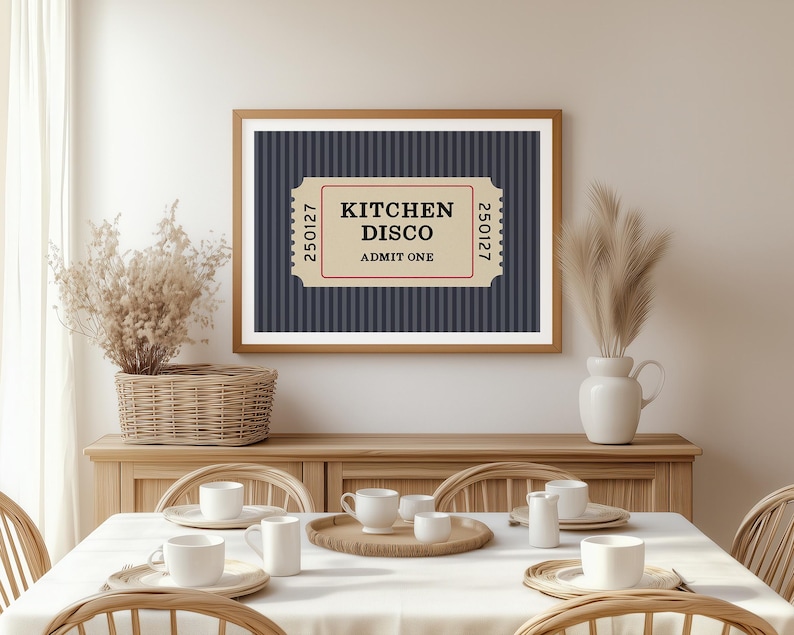 Puede incluir: Un cuadro enmarcado con un marco de madera marr&oacute;n que presenta un dise&ntilde;o de boleto que dice "KITCHEN DISCO ADMIT ONE" sobre un fondo a rayas azul marino. El cuadro se exhibe sobre un mueble de madera, con una mesa de comedor.