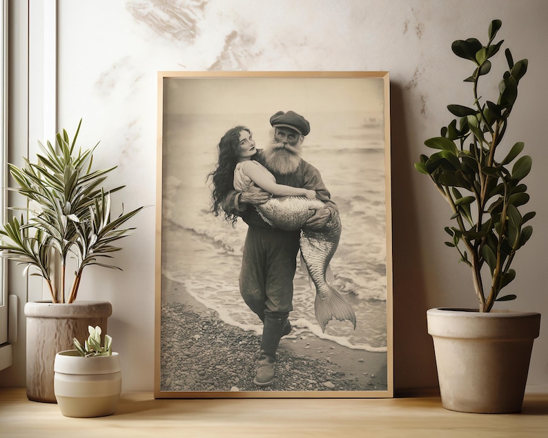 K&ouml;nnte beinhalten: Ein Schwarzwei&szlig;-Foto aus der Vintage-Zeit, das einen b&auml;rtigen Mann zeigt, der eine Meerjungfrau in seinen Armen h&auml;lt. Der Mann tr&auml;gt einen Matrosenhut und eine dunkle Jacke. Die Meerjungfrau tr&auml;gt einen Muschelbh und hat langes, flie&szlig;endes Haar. Das Foto ist vor einem Strandhintergrund aufgenommen.