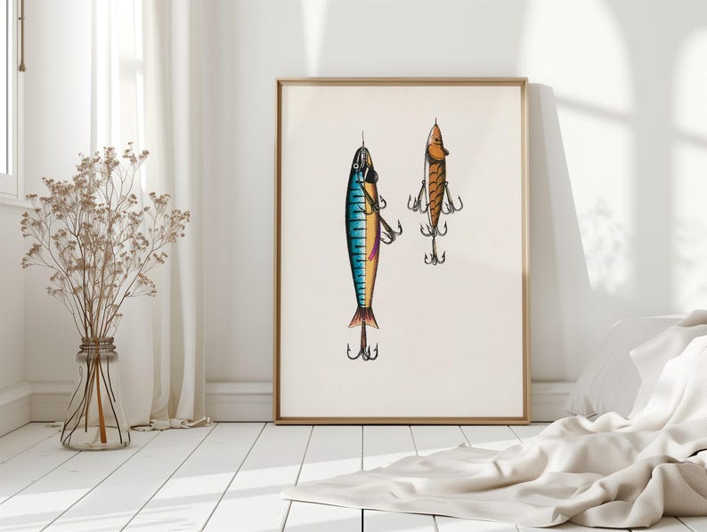May include: A framed print featuring two detailed illustrations of fishing lures. One lure is blue, yellow, and pink, while the other is orange. Both lures have multiple hooks and are set against a cream-colored background.