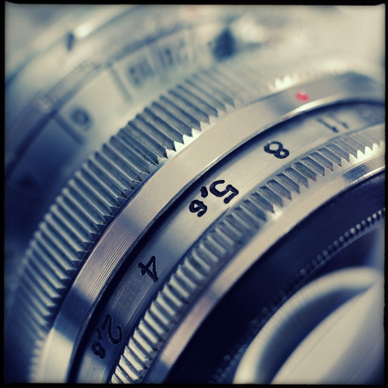 May include: Close-up of a silver camera lens with a depth of field scale marked with numbers 2, 4, 5.6, 8, and 11.