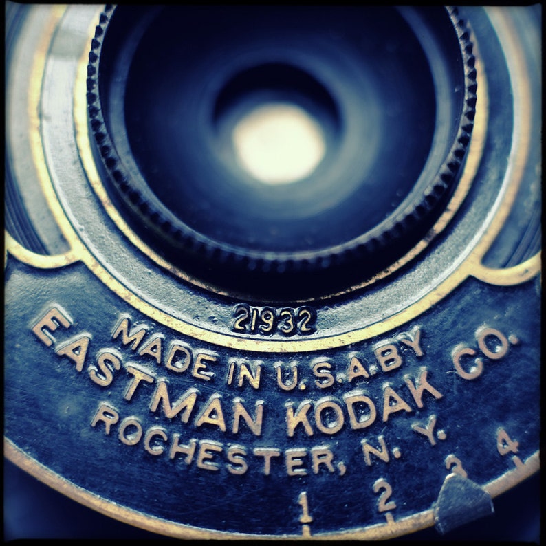 May include: Close-up of a vintage camera lens with the text "MADE IN U.S.A. BY EASTMAN KODAK CO. ROCHESTER, N.Y." and the number "21932" printed on the metal.
