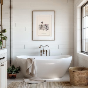 May include: A modern bathroom with a white, oval-shaped bathtub. A framed vintage print hangs above the tub. A woven basket and potted plant add natural elements. A beige towel is draped over the tub's edge. The walls are white.