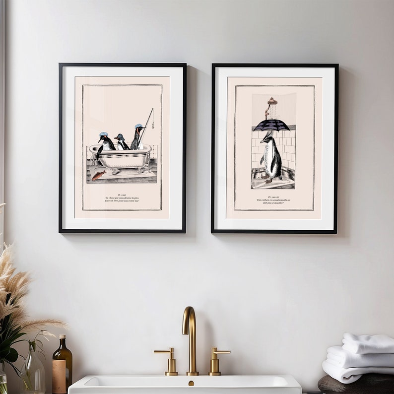 May include: Two framed art prints with penguin illustrations. One shows penguins in a bathtub, the other a penguin under a shower. Both prints have black frames and include text at the bottom. The art has a vintage, whimsical style.
